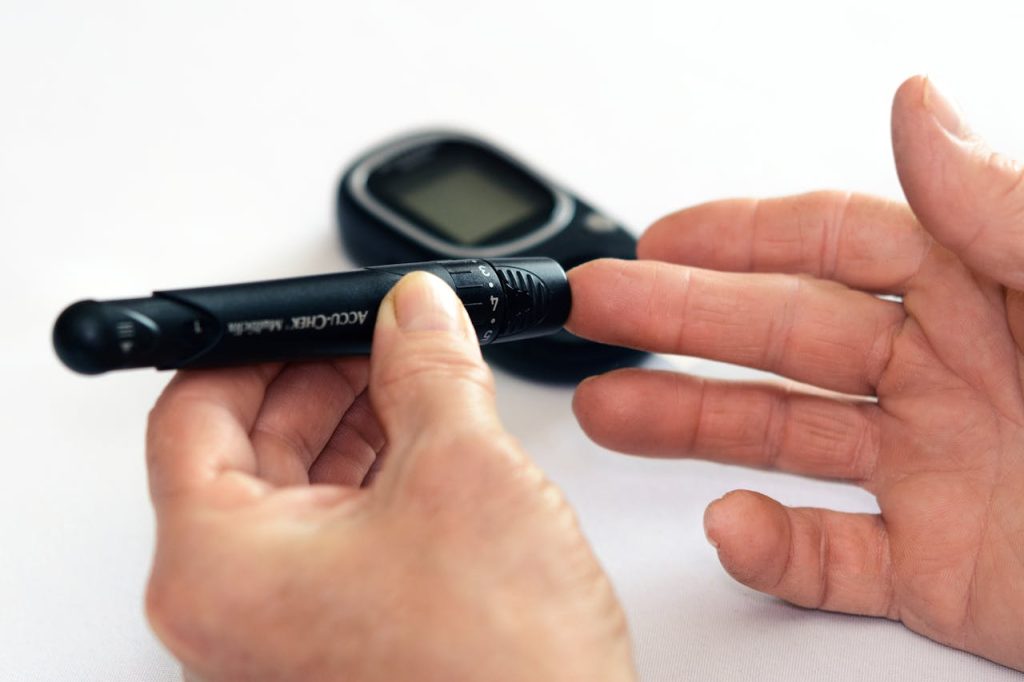 person-holding-black-tube-1001897 Close-up image of a person using a glucometer for diabetes management indoors.